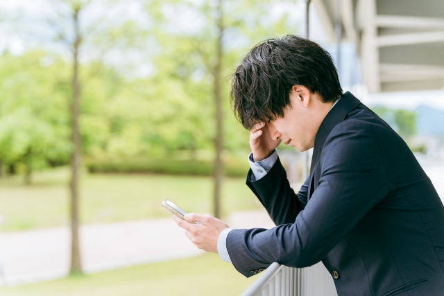 スマホを片手に落ち込んでいる男性