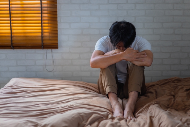 ベットの上でうずくまる男性