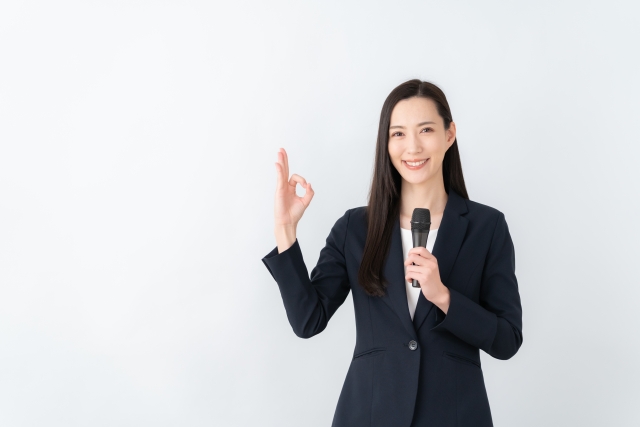 片手でマイクを持ってもう片手でOKサインをしている女性
