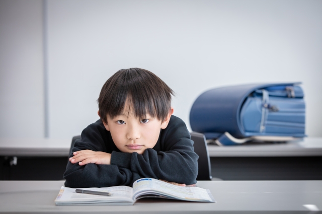 机に寄っかかっている男の子とランドセル