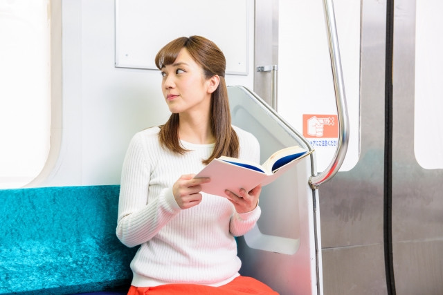 横を見ながら電車で本を読んでいる女性