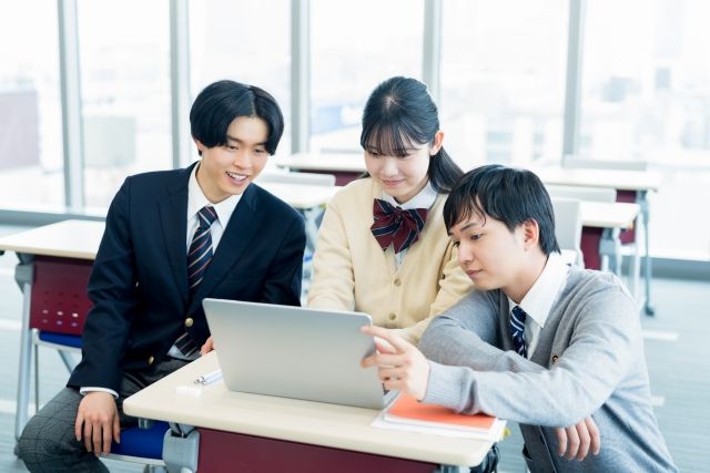 パソコンを眺めて会話する3人の高校生